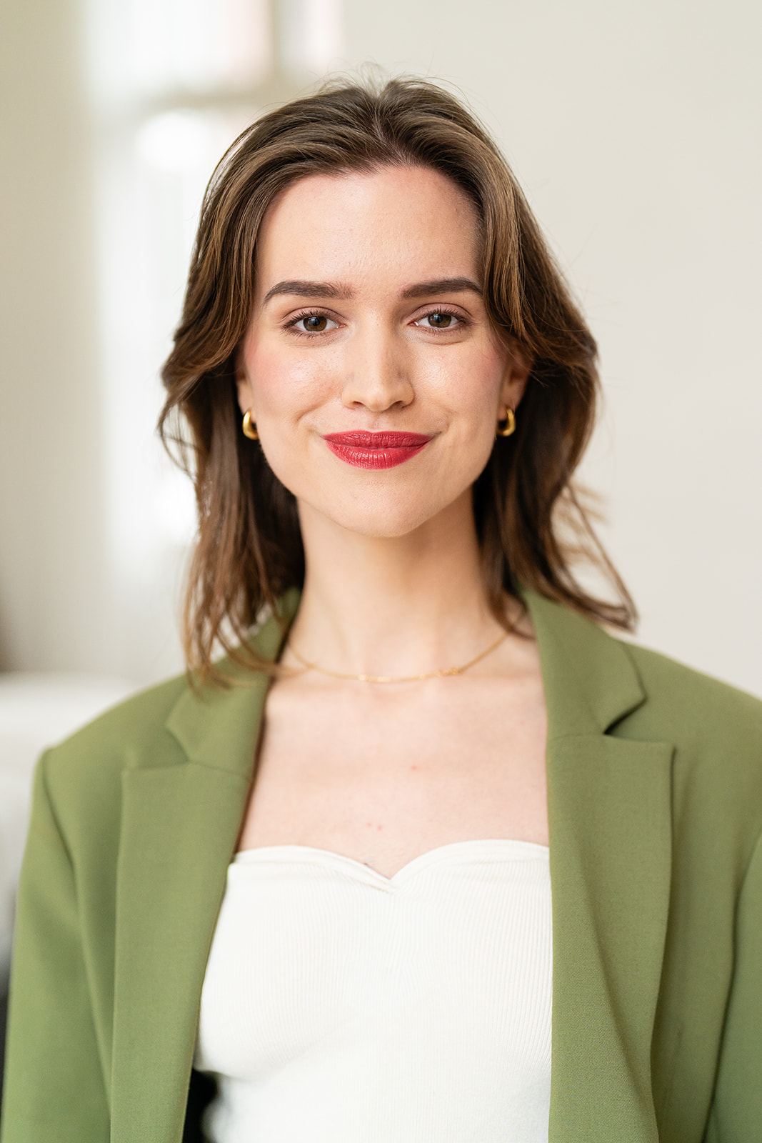 The same model in a green blazer with gold jewelry and red lipstick